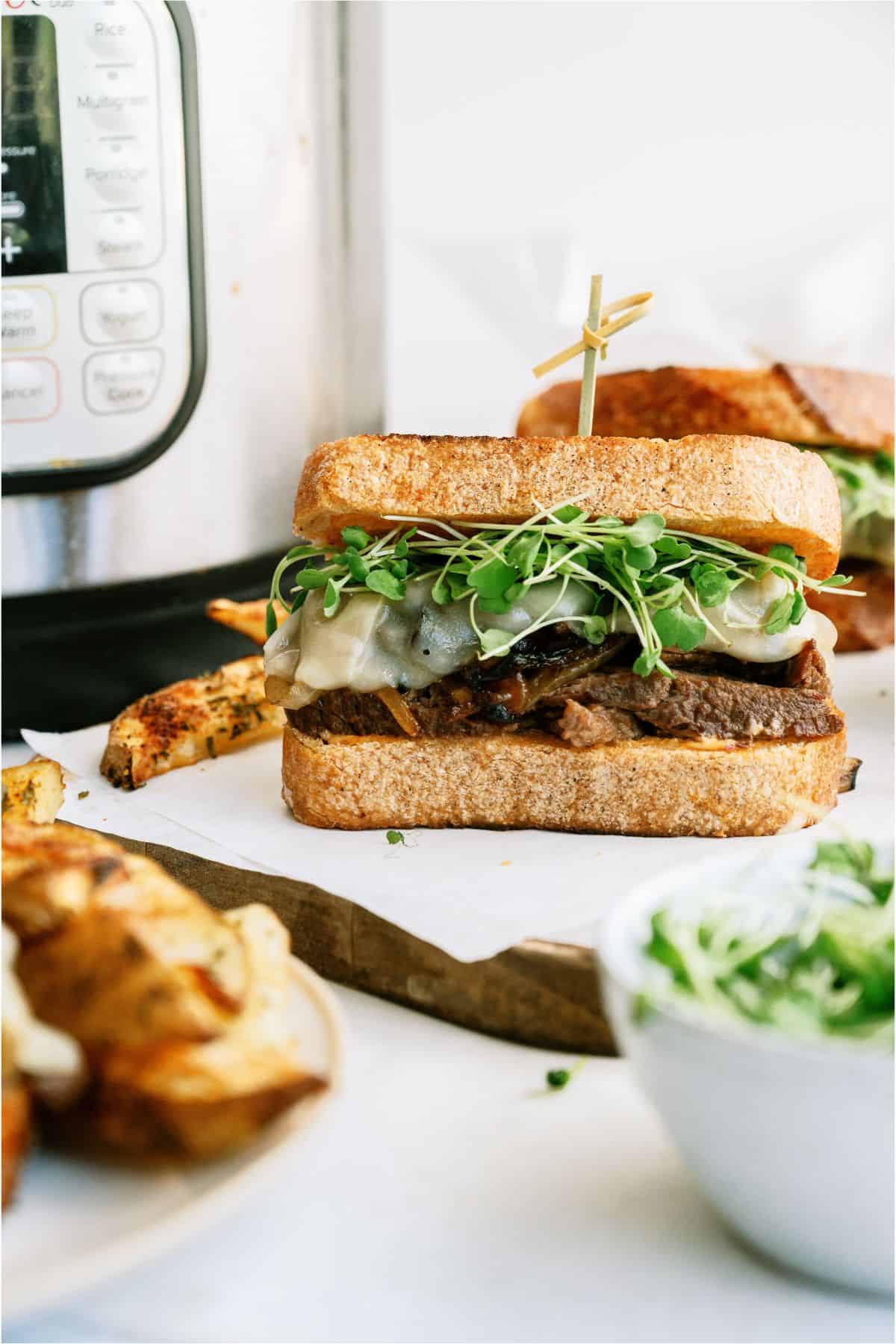 An Instant Pot Pot Roast Sandwich on s cutting board with an Instant Pot in the back ground