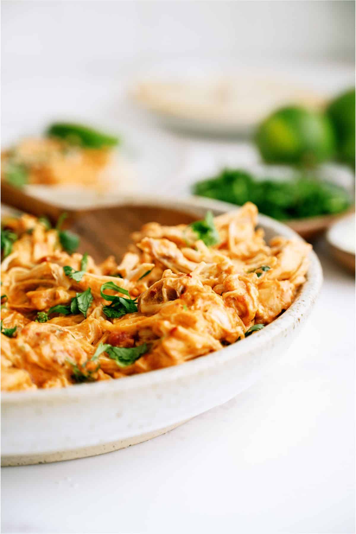 A bowl with Slow Cooker Queso Chicken and a wooden spoon