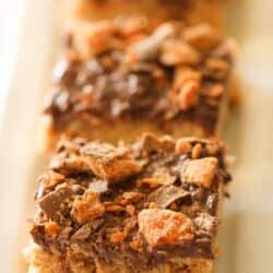 A close-up of three slices of dessert bars with a crumbly base, a chocolate topping, and bits of crushed candy pieces.