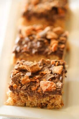 A close-up of three slices of dessert bars with a crumbly base, a chocolate topping, and bits of crushed candy pieces.