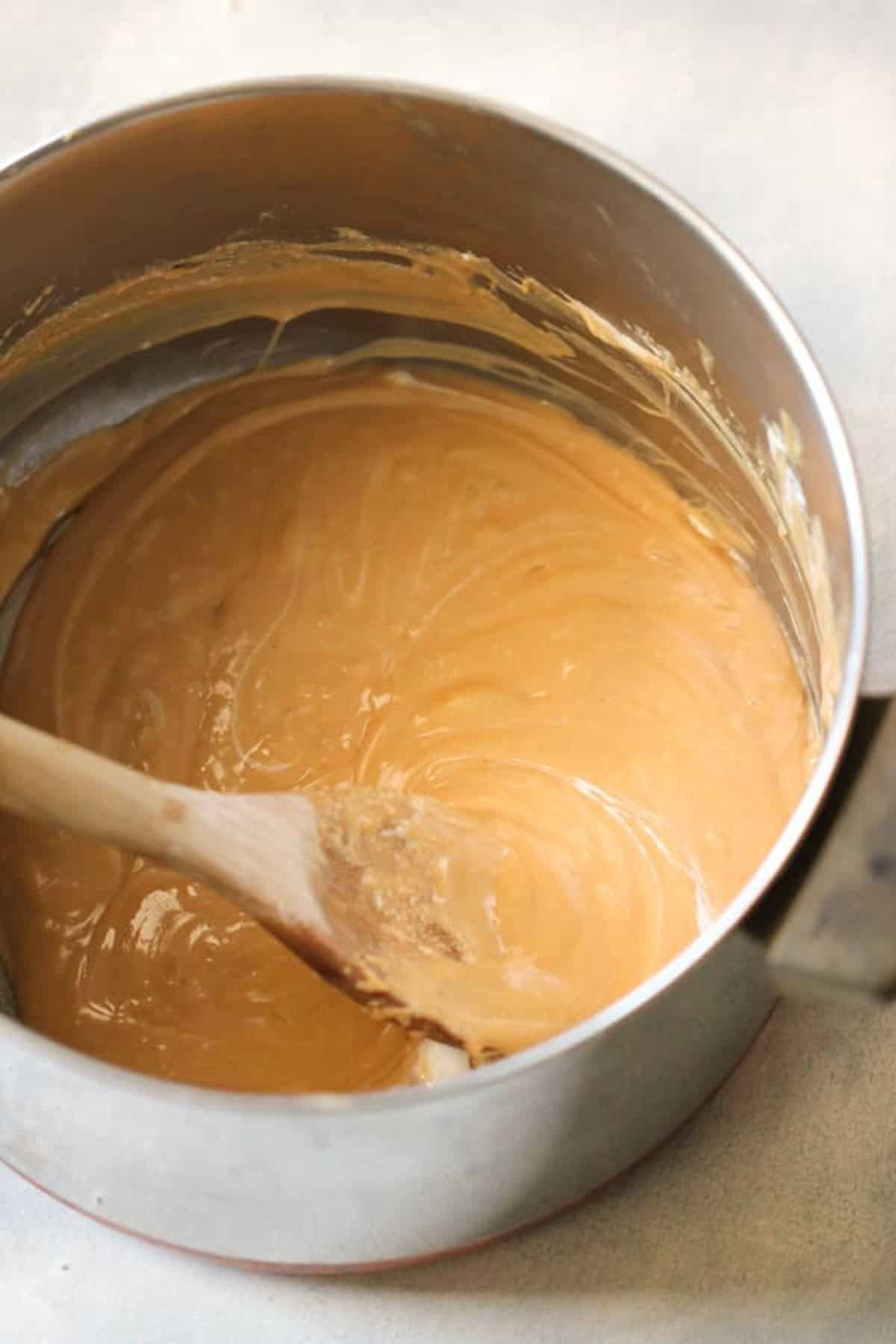 A saucepan with smooth, light brown caramel sauce being stirred with a wooden spoon.