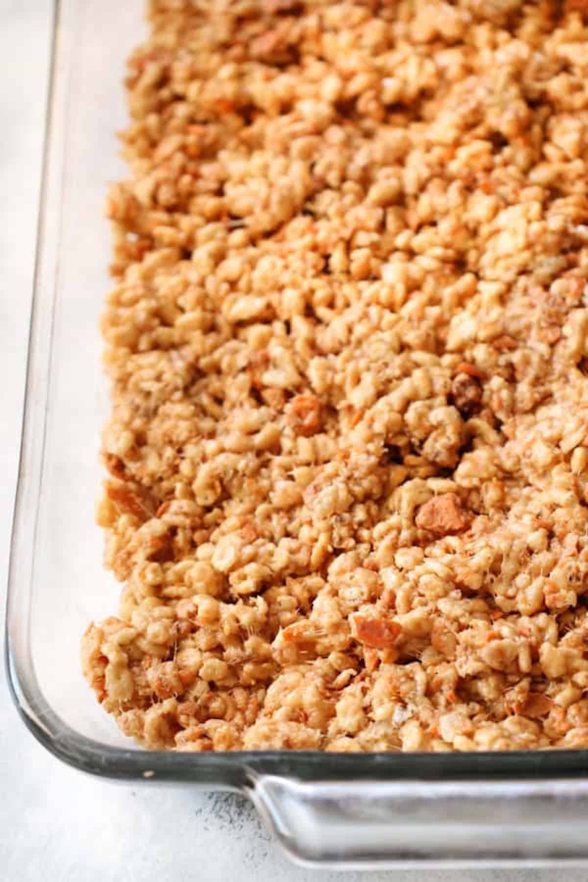 A glass baking dish filled with a baked, crumbly mixture of oats and cereal resembling a granola or crisp topping. The close-up shot highlights its golden-brown, crunchy texture.