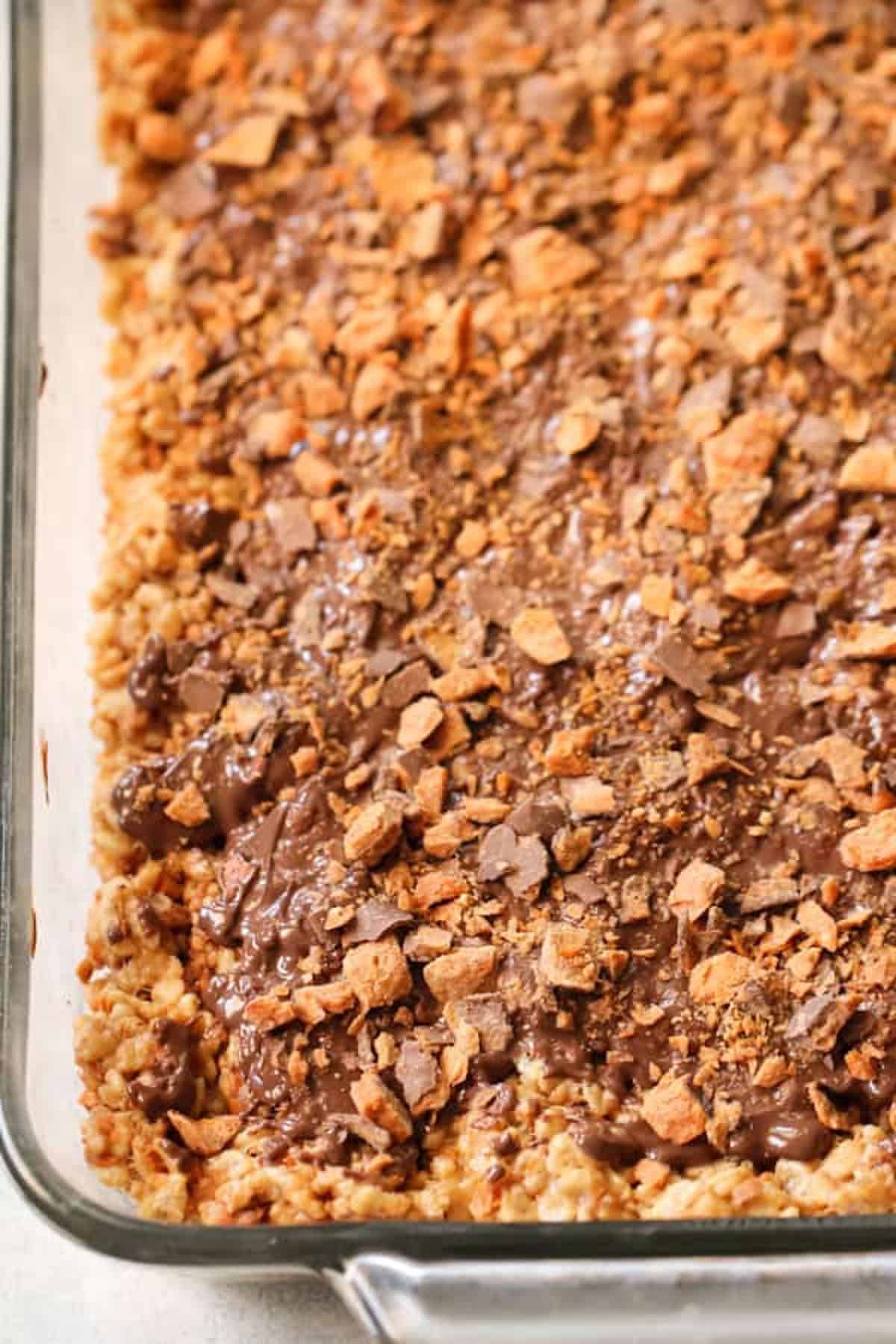 A close-up view of a glass baking dish filled with chocolate-covered crispy rice cereal bars topped with crushed wafer pieces.