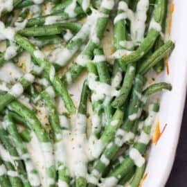 A dish of cooked green beans topped with melted cheese on a white rectangular serving plate.