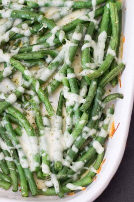 A dish of cooked green beans topped with melted cheese on a white rectangular serving plate.