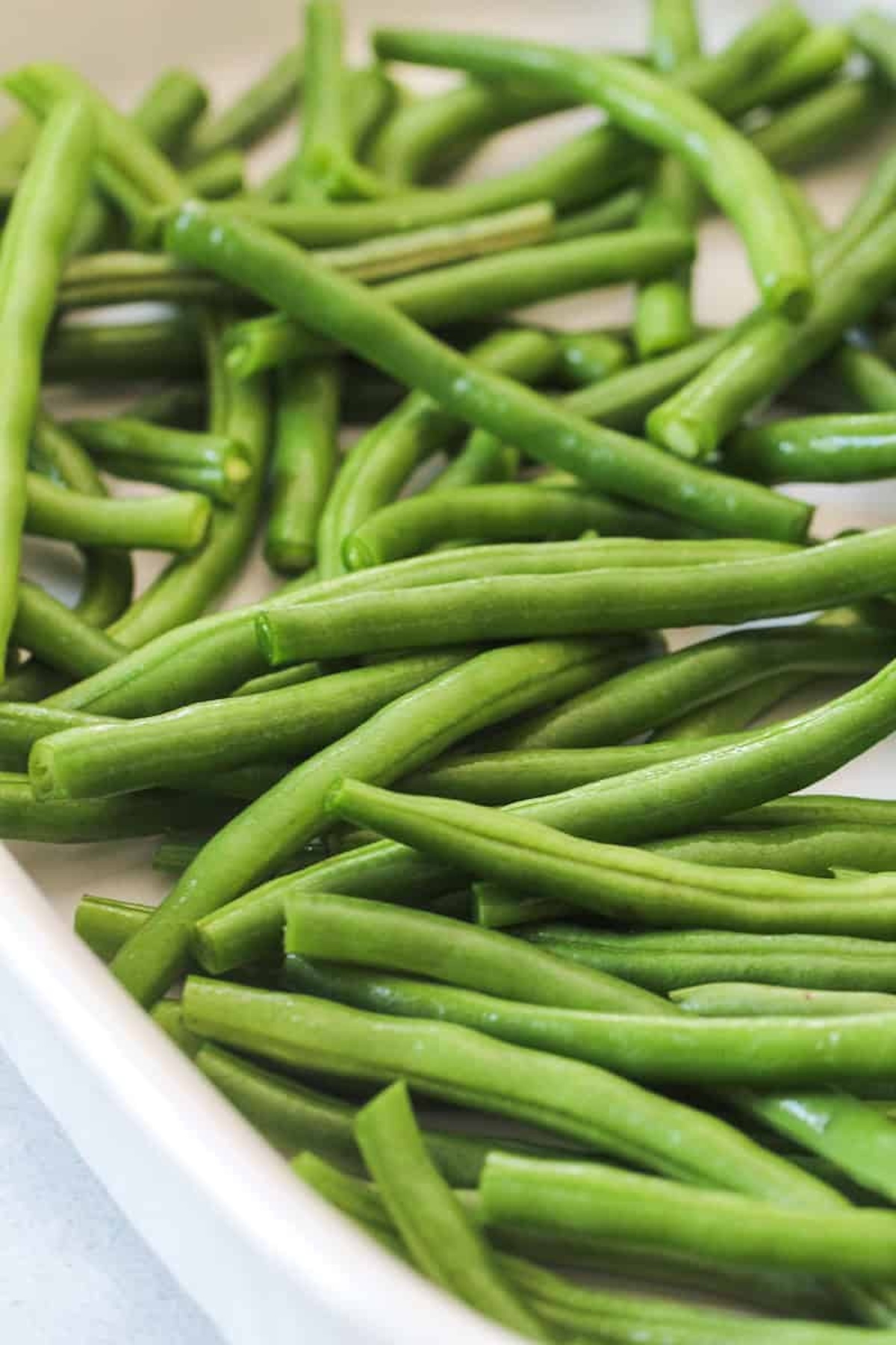 A close-up view of fresh green beans piled together in a white dish.