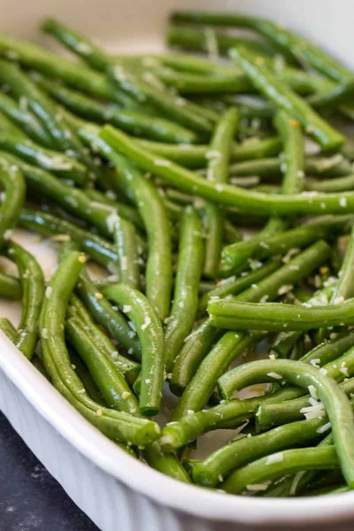 A white dish filled with cooked green beans, garnished with grated cheese.