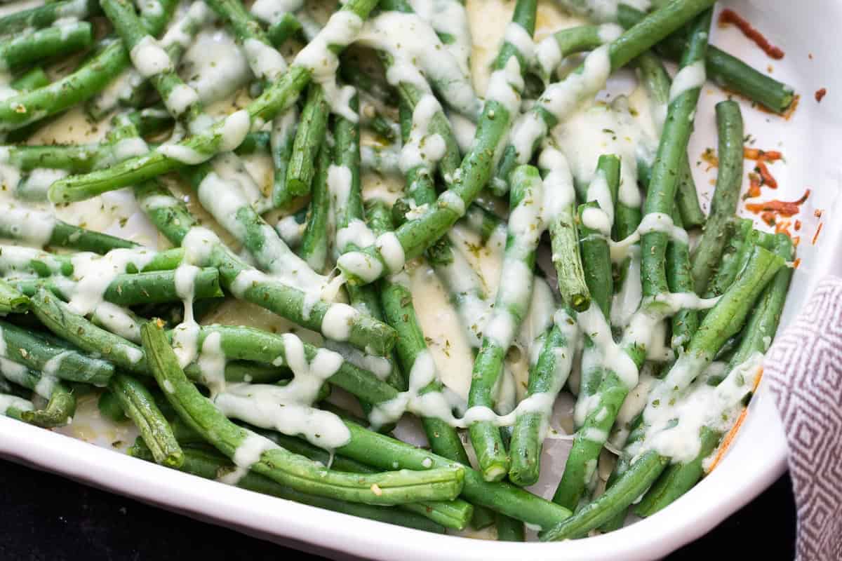 A dish of cooked green beans topped with melted cheese in a white baking dish.