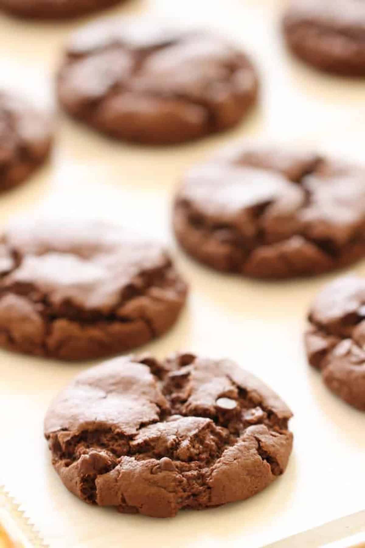 Close-up of nine chocolate cookie dough balls evenly spaced on a parchment-lined baking sheet.