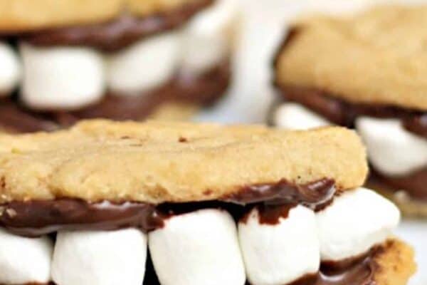Three cookie sandwiches filled with marshmallows and chocolate, resembling smiling mouths with teeth, are placed on a white plate.