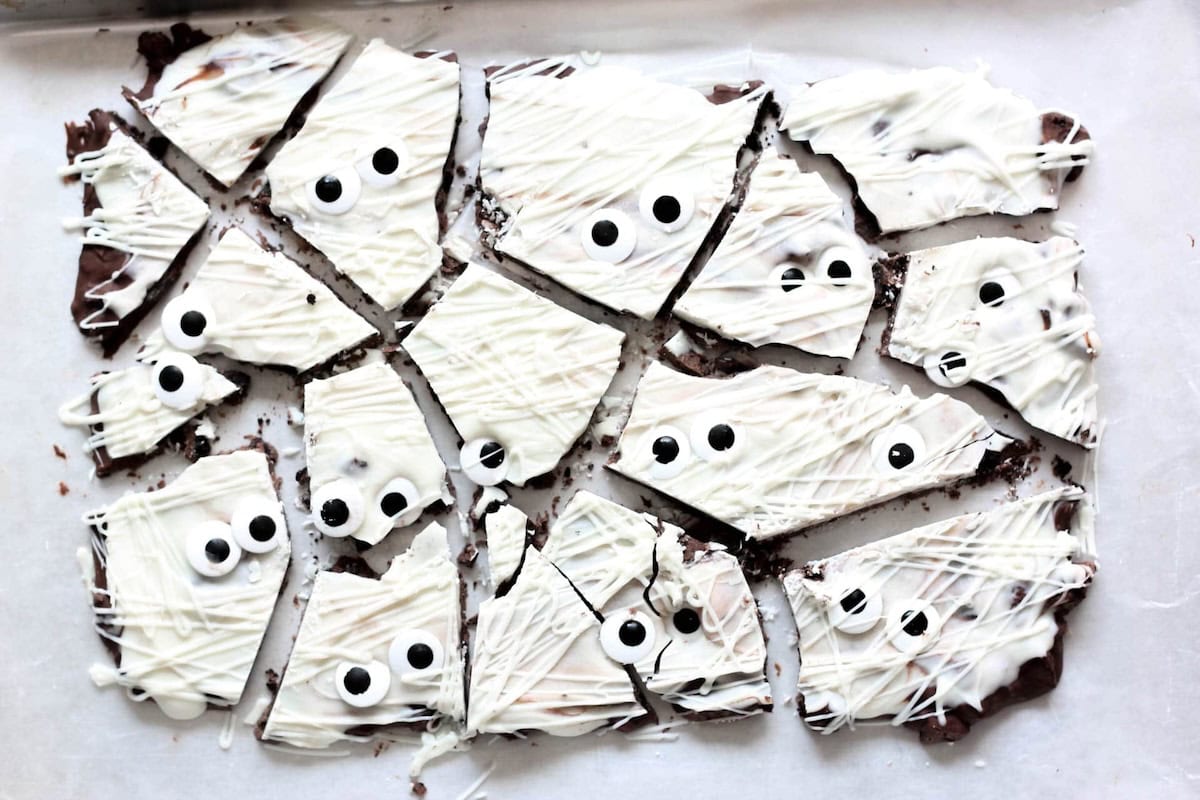 A tray of broken chocolate bark pieces topped with white chocolate and candy eyes, designed to resemble mummies.