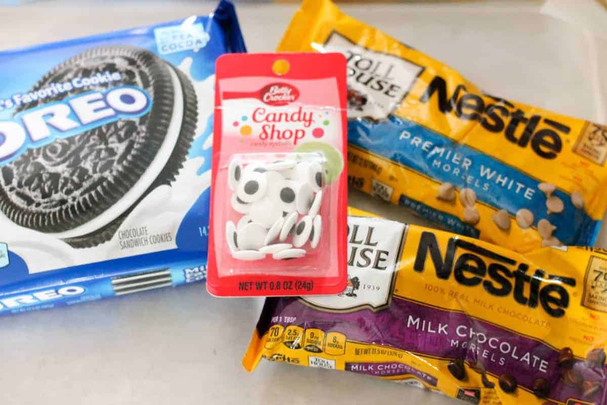 A pack of Oreo cookies, a packet of Betty Crocker candy eyes, and bags of Nestle Toll House premier white morsels and milk chocolate morsels are arranged on a countertop.