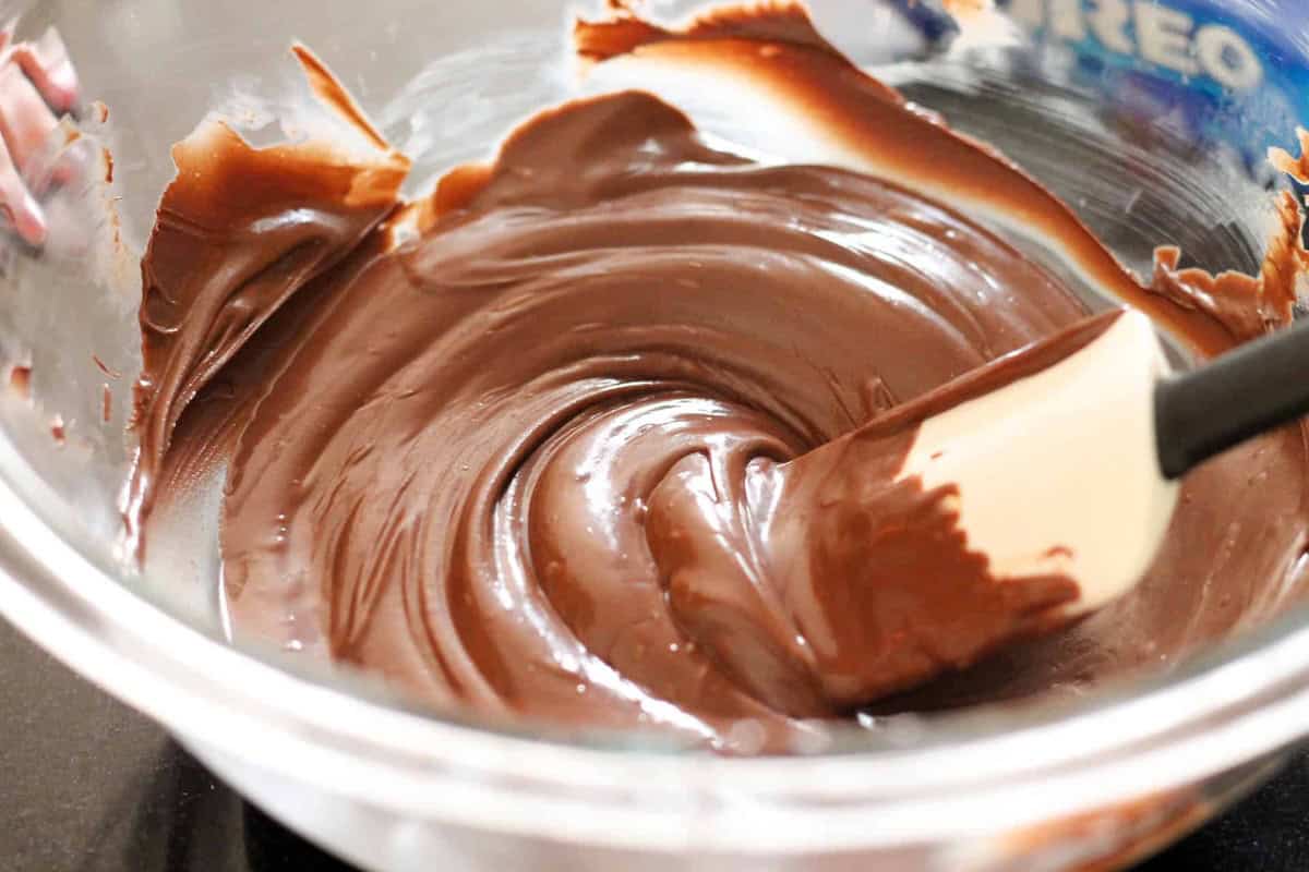 Close-up of a glass bowl containing smoothly stirred melted chocolate with a white and black spatula resting in it.