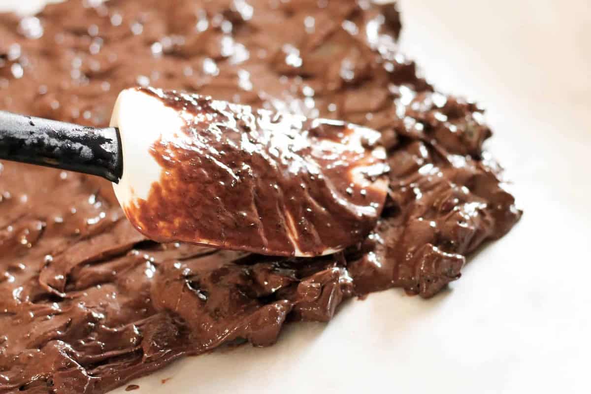 A spatula spreads melted dark chocolate on a flat surface.