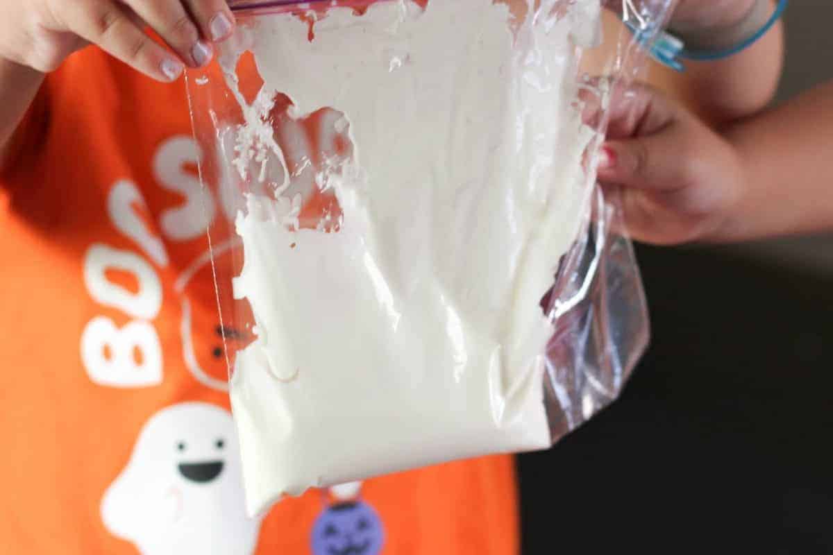 Child holding a plastic ziplock bag filled with white liquid substance. The child is wearing an orange shirt.