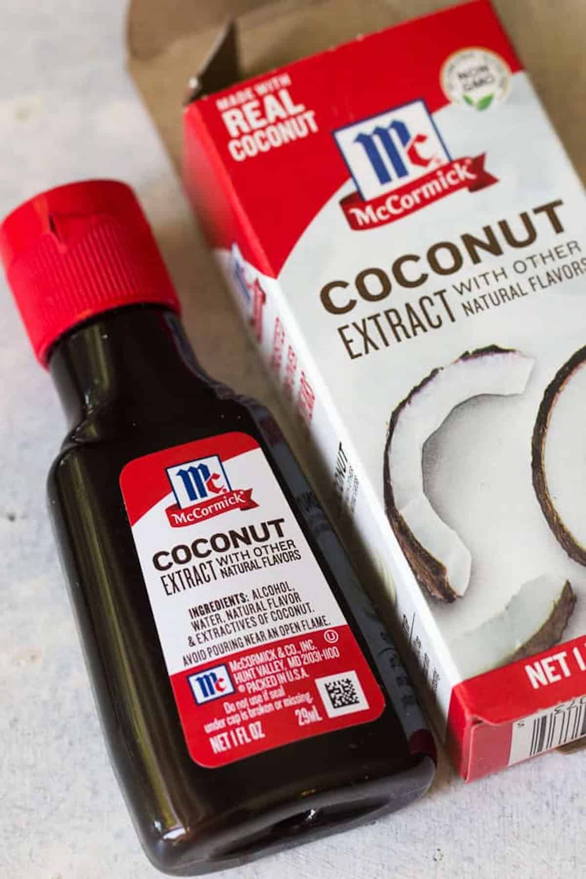 A bottle and its box of McCormick Coconut Extract with other natural flavors, made with real coconut. The bottle is dark and labeled, placed next to the red and white box featuring coconut images.