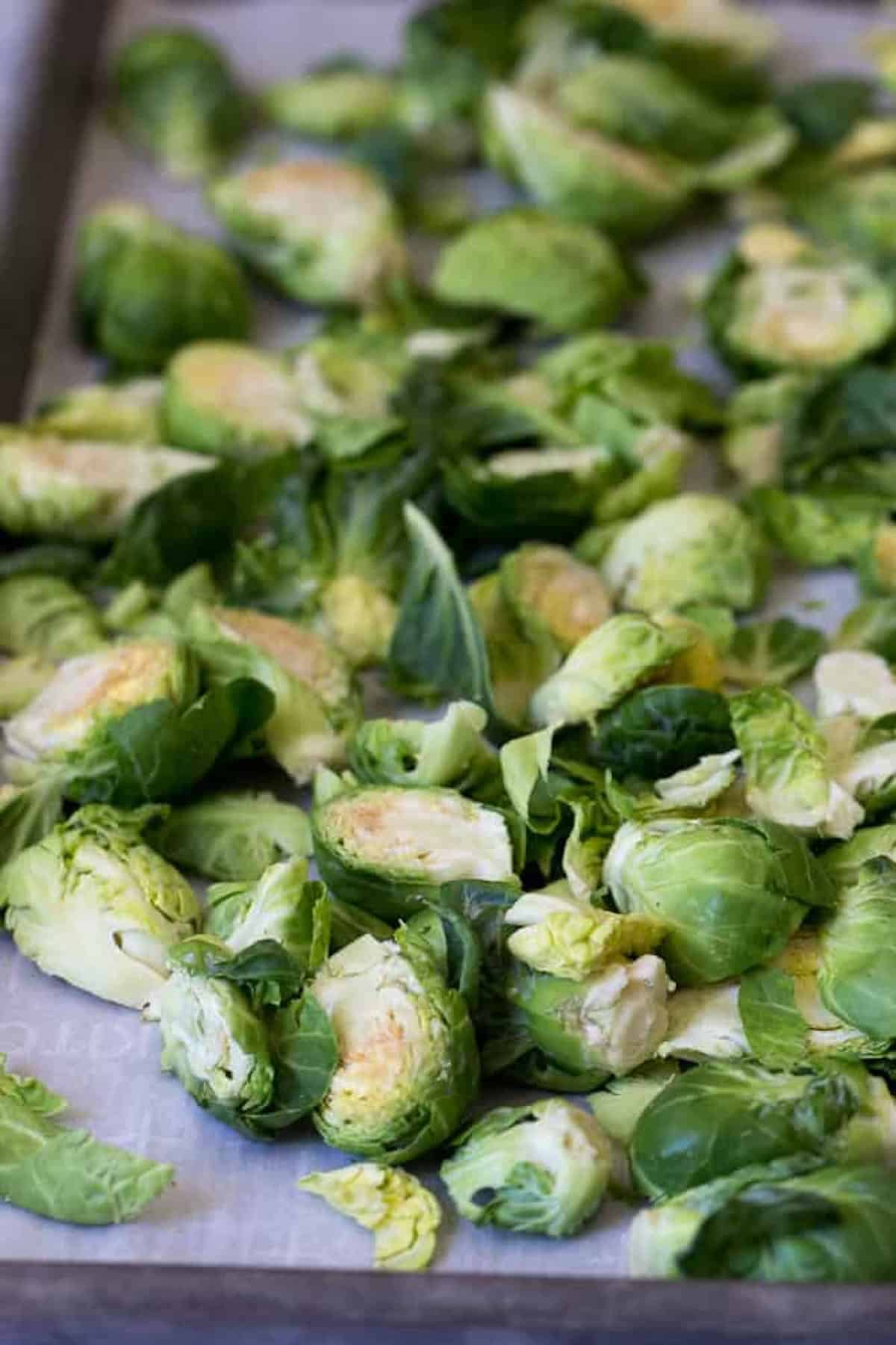 A tray of halved Brussels sprouts prepared for roasting, displayed on parchment paper.