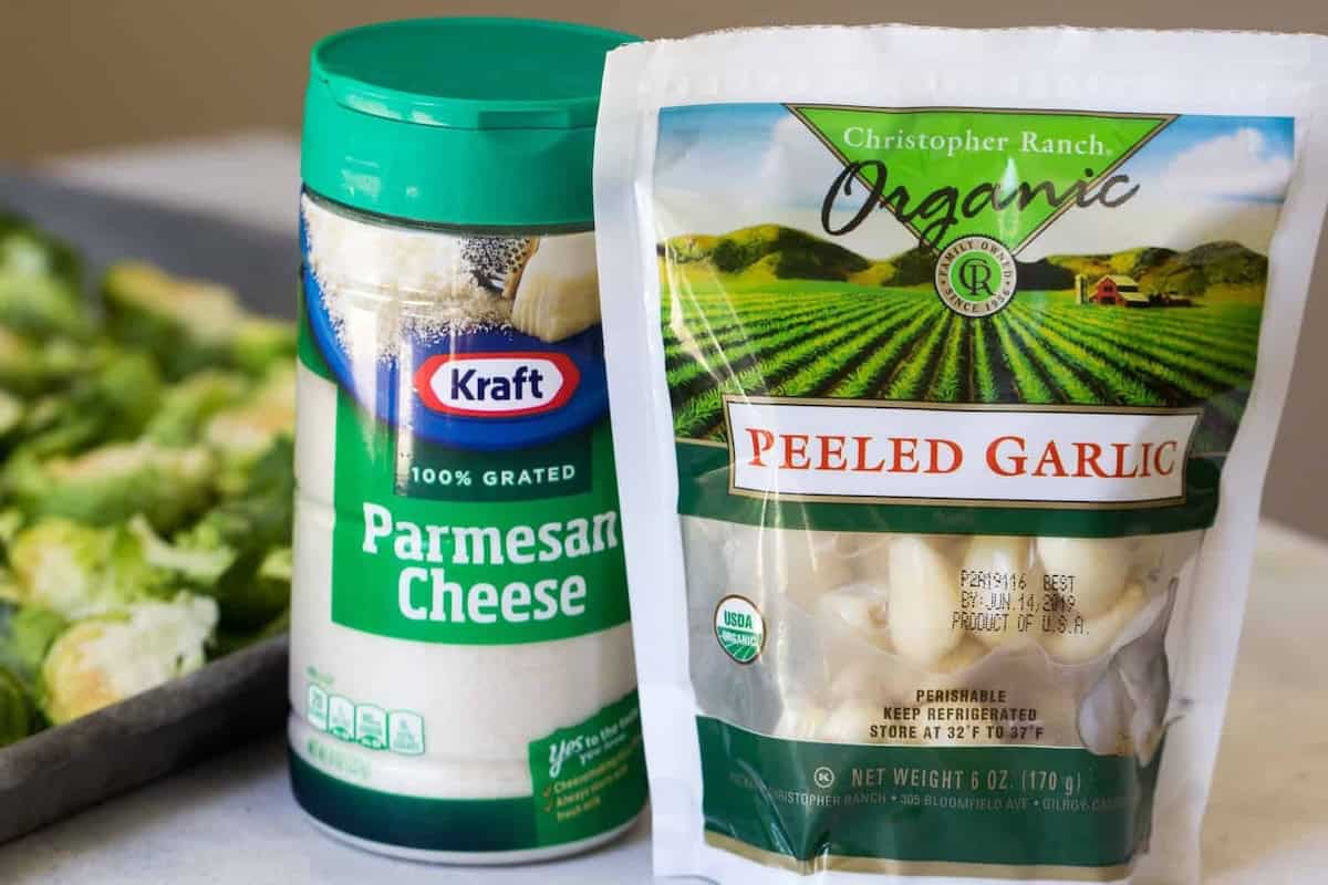 A container of Kraft 100% Grated Parmesan Cheese and a bag of Christopher Ranch Organic Peeled Garlic are displayed in front of a tray of chopped vegetables.