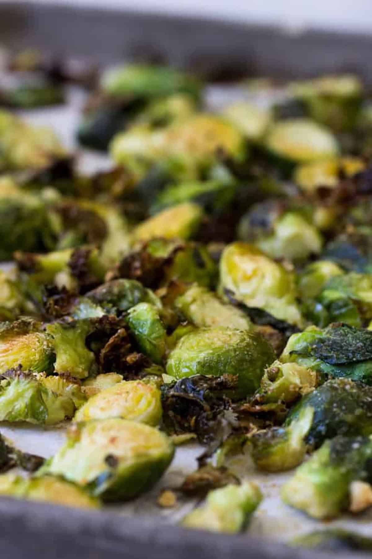 Close-up of roasted Brussels sprouts on a baking sheet, showing a mix of charred and golden-brown pieces.