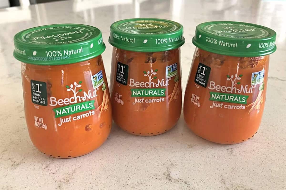 Three jars of Beech-Nut Naturals "Just Carrots" baby food placed on a countertop. Each jar has a green lid and a clear label indicating the contents are 100% natural.