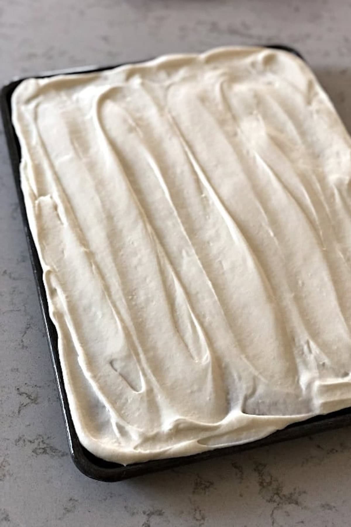 A rectangular baking pan filled with a smooth, uncooked layer of cream or batter is placed on a countertop.