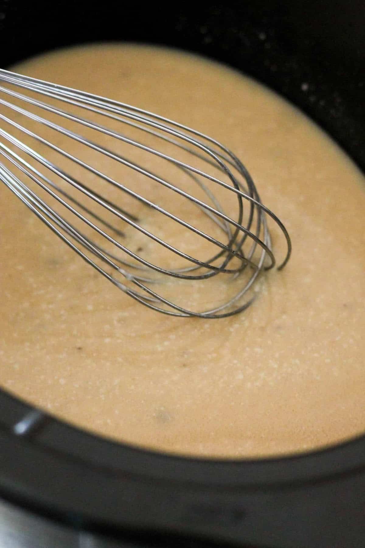 A whisk stirring a light brown mixture in a black pot.