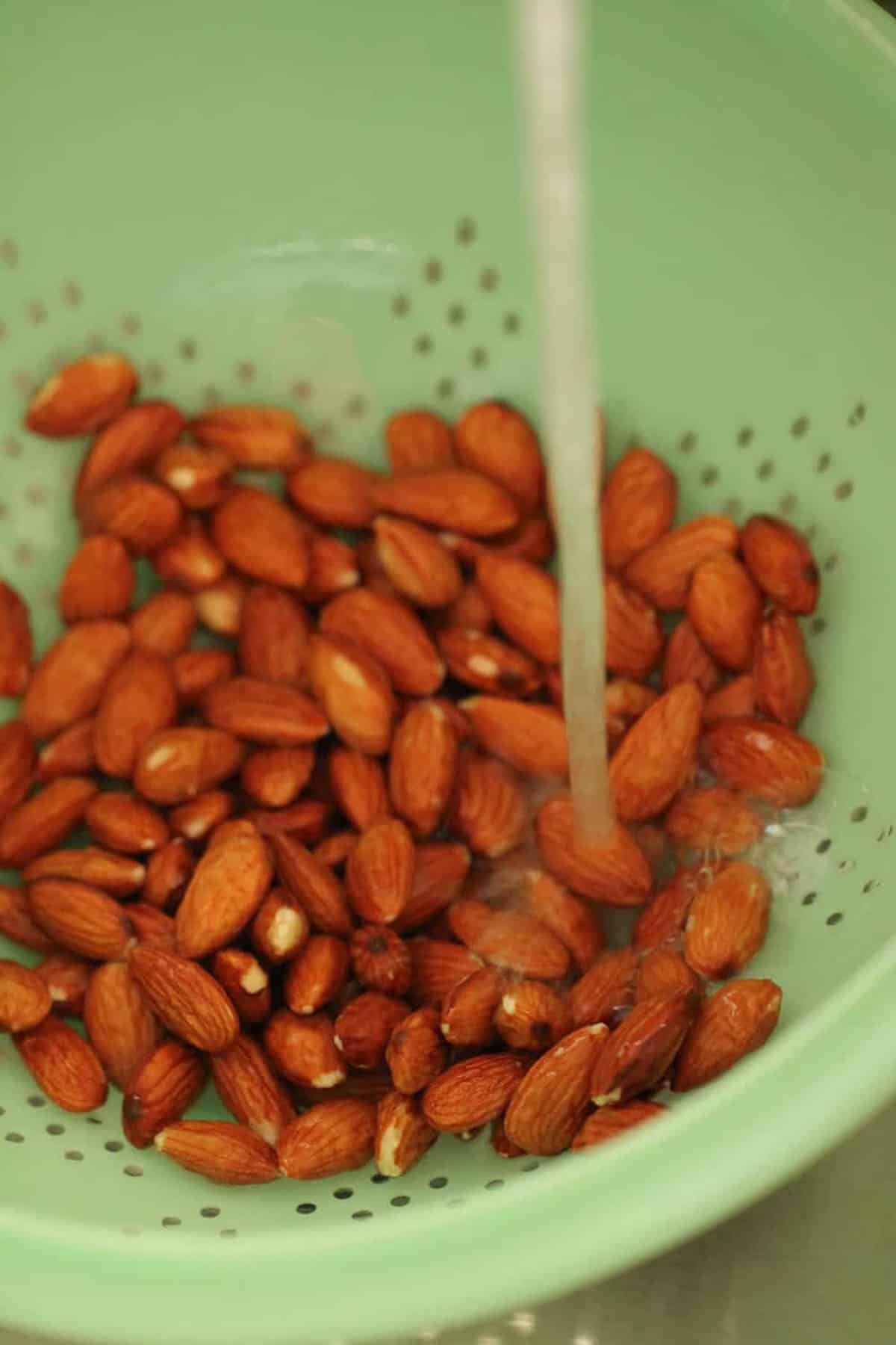 A stream of water falls onto a pile of almonds in a green colander.