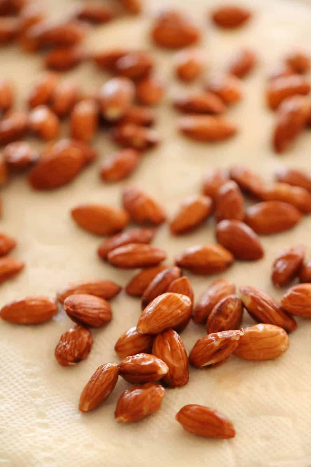 A close-up of several blanched almonds spread out on a white textured surface.