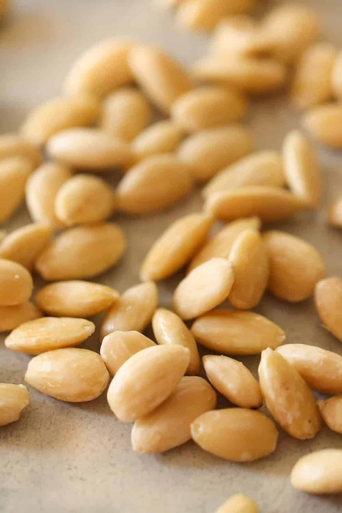 Close-up image of scattered blanched almonds on a light surface. The almonds have a smooth, pale appearance without their skins.