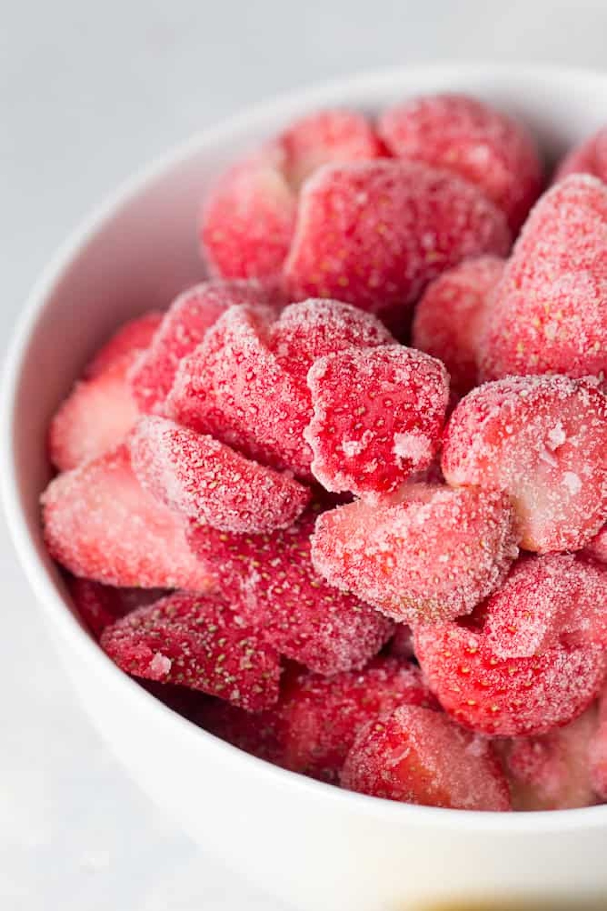 A white bowl filled with frozen, sliced strawberries covered in frost.