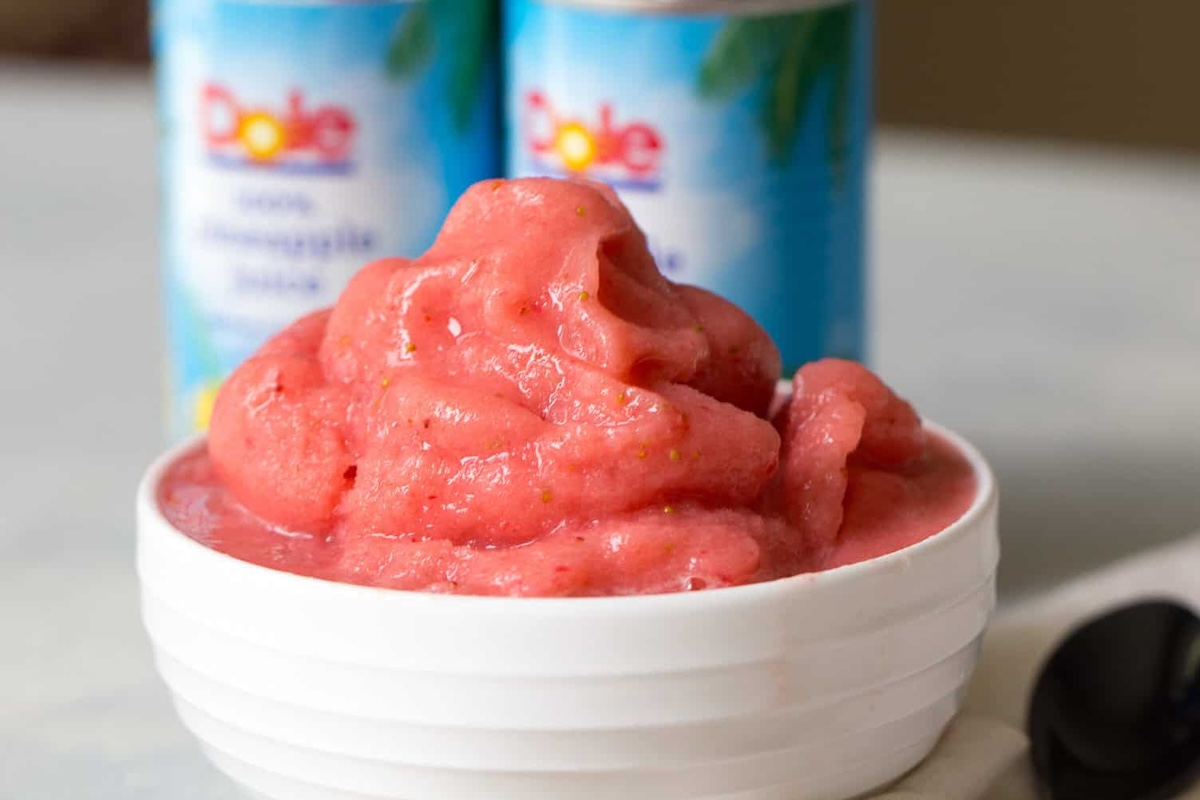A bowl of pink fruit sorbet with a smooth texture is in front of two coconut milk cans labeled "Dole.