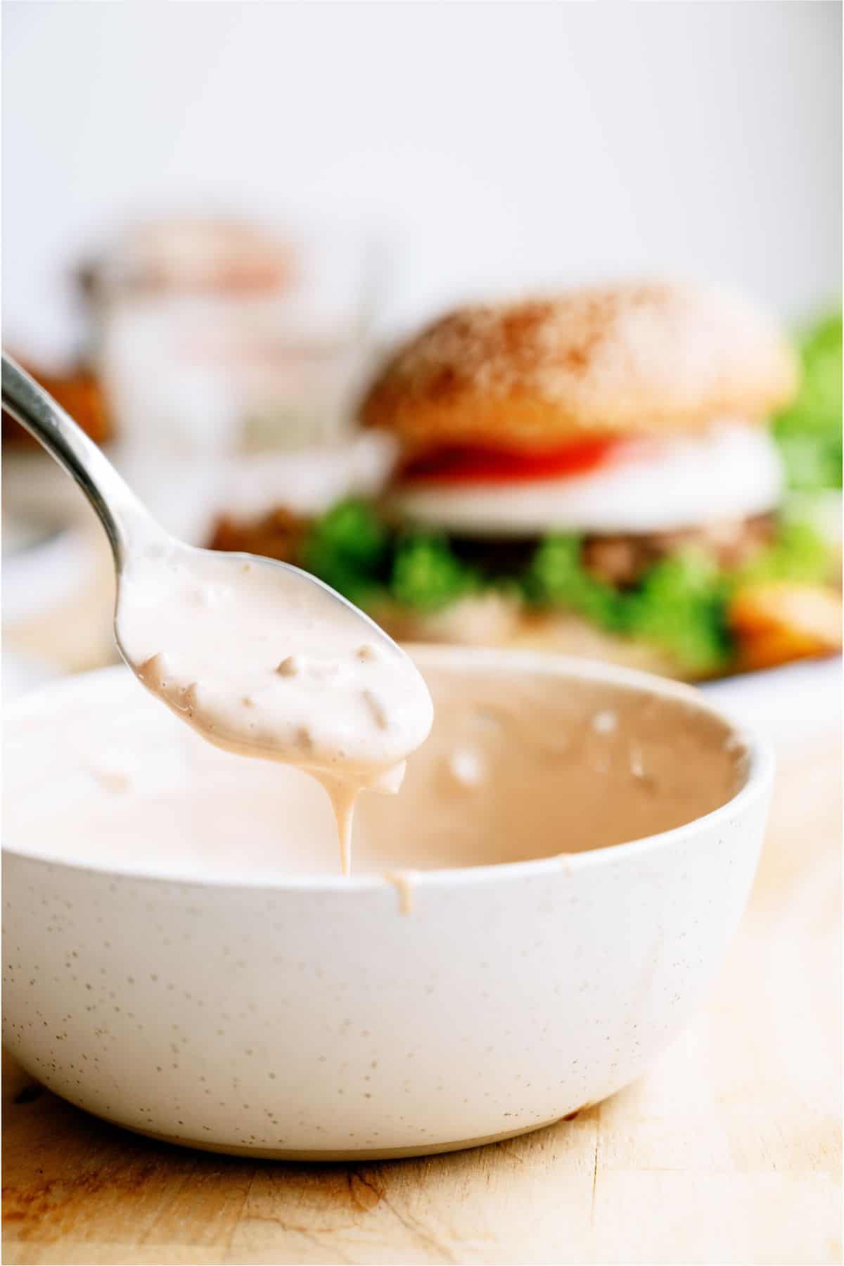 A bowl of secret sauce with a spoon and a Best Hamburger Recipe With Famous Secret Sauce in the background