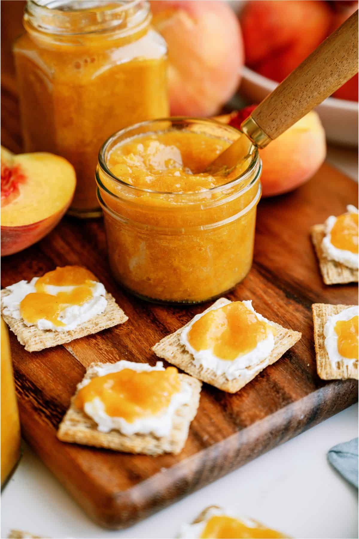 Instant Pot Peach Preserves in a jar with crackers surrounding it topped with Instant Pot Peach Preserves