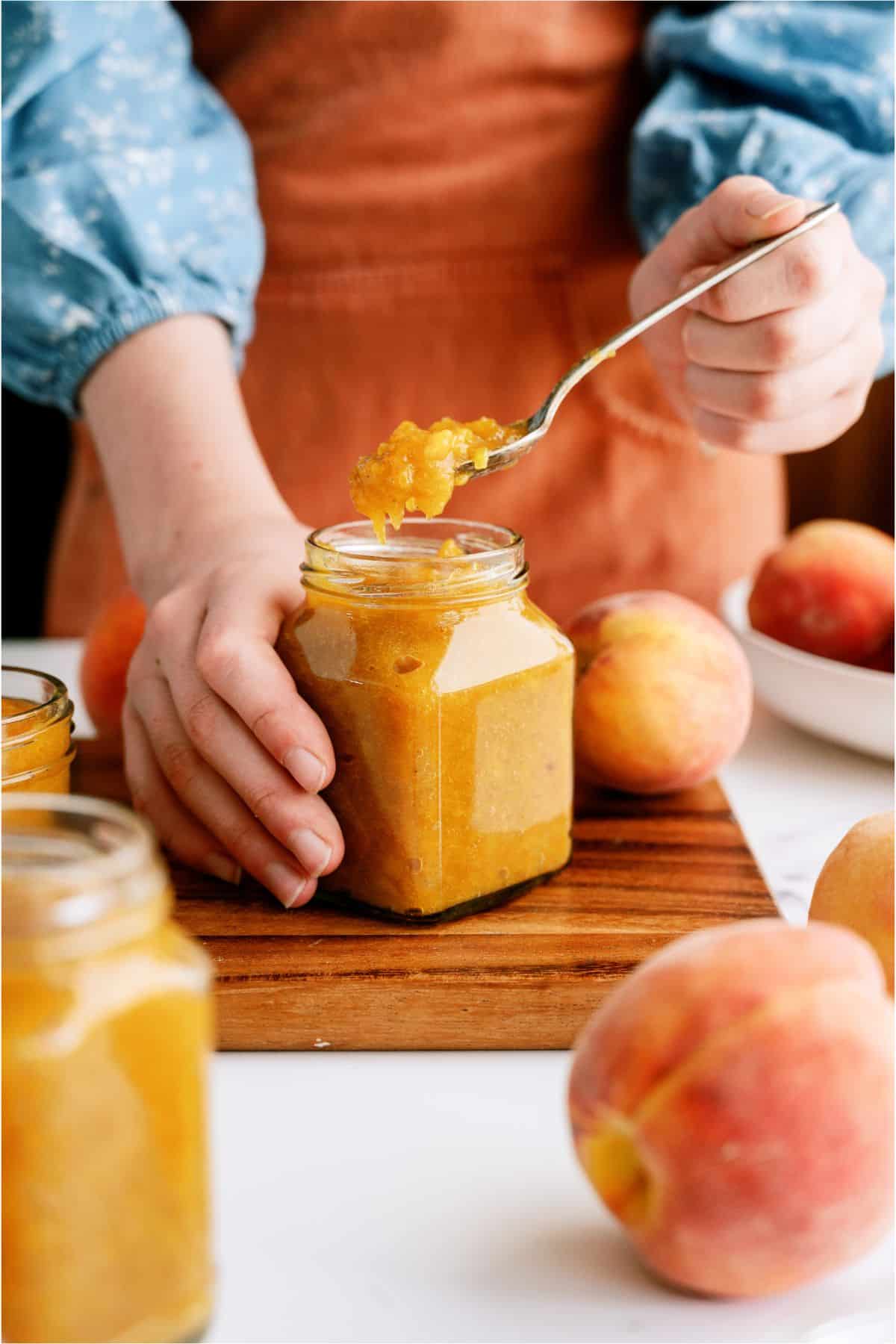 Instant Pot Peach Preserves in a jar with someone lifting a spoonful out