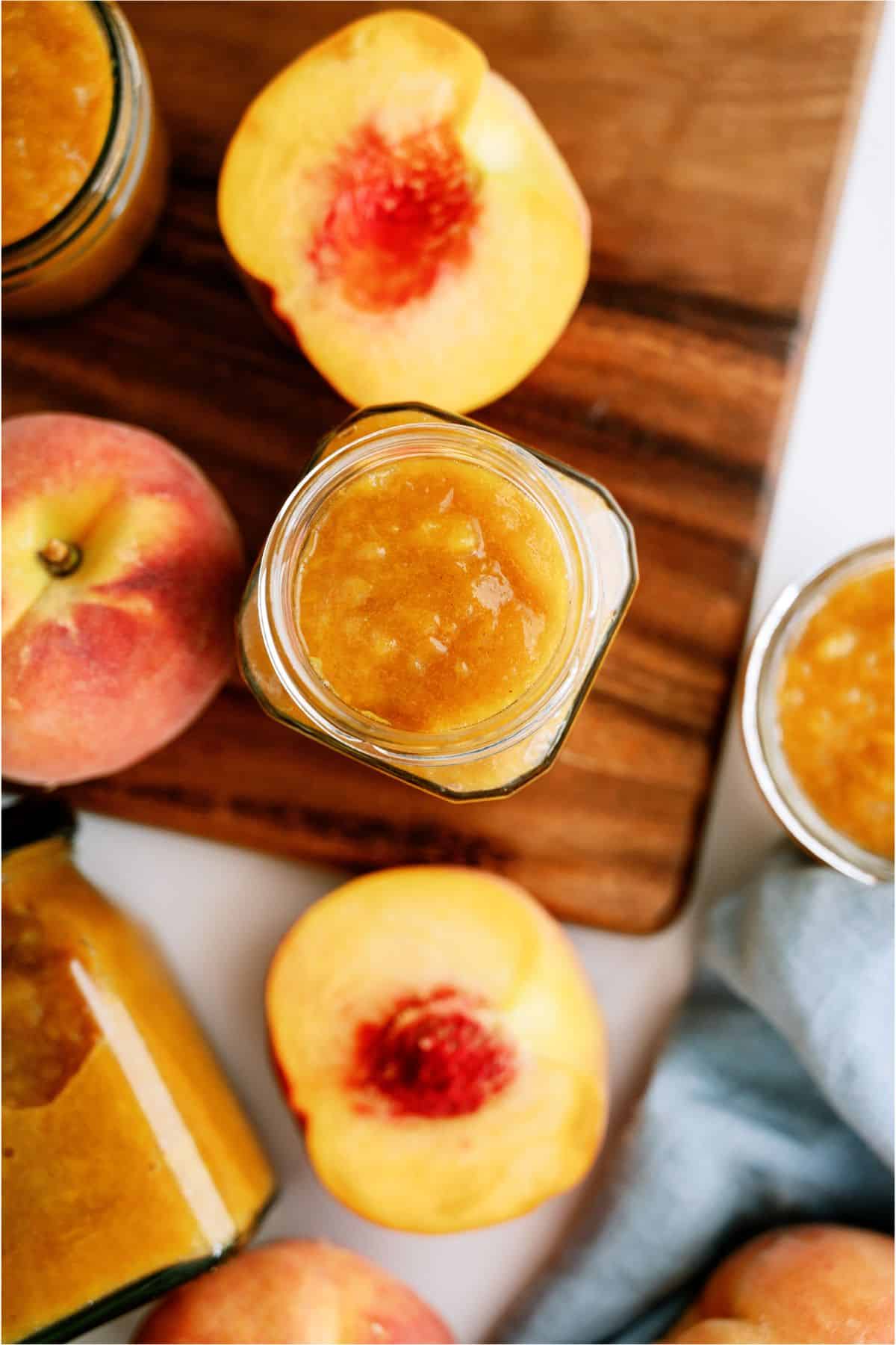 Top view of a jar of Instant Pot Peach Preserves and fresh cut peaches