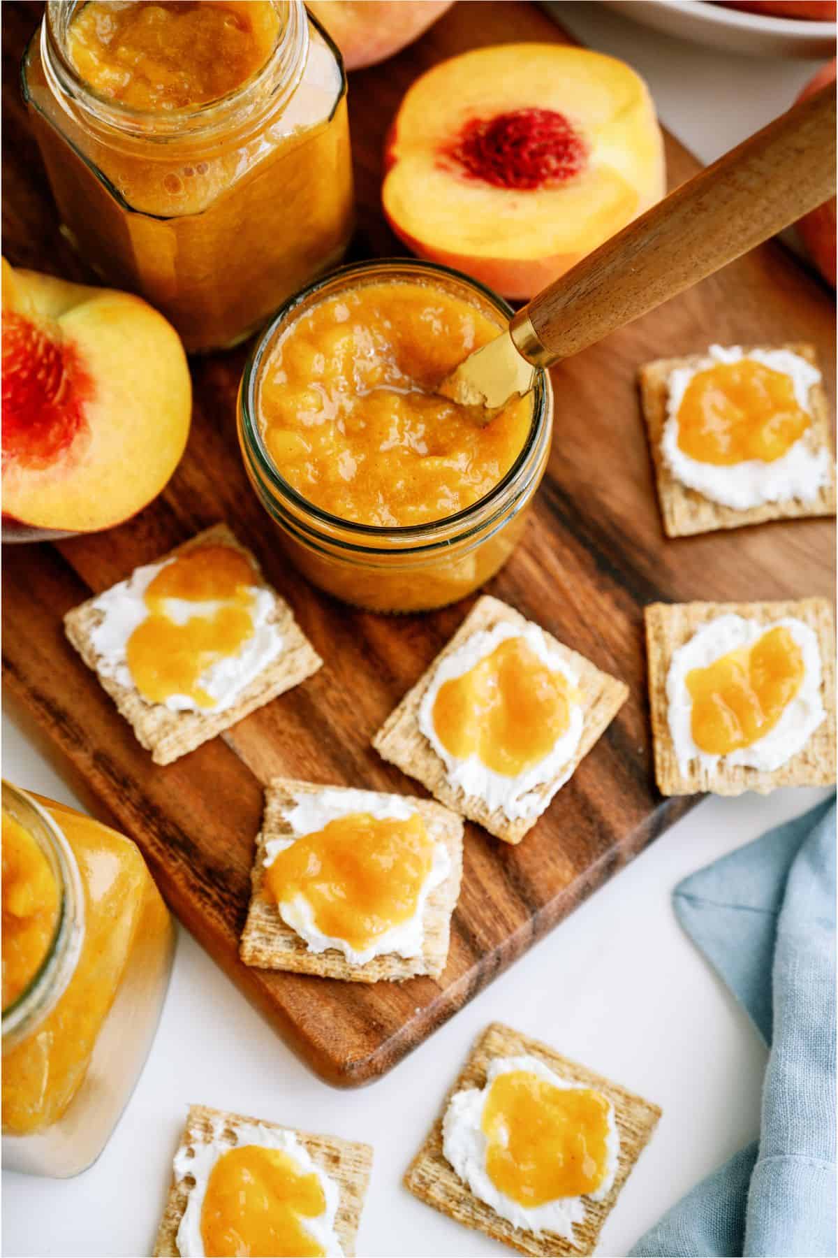 A jar of Instant Pot Peach Preserves surrounded by crackers topped with peach preserves