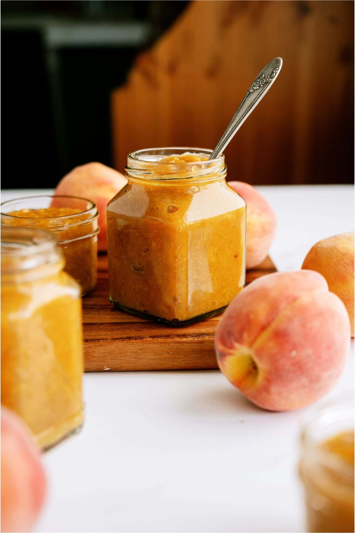 Instant Pot Peach Preserves in a jar with a spoon surrounded by fresh peaches