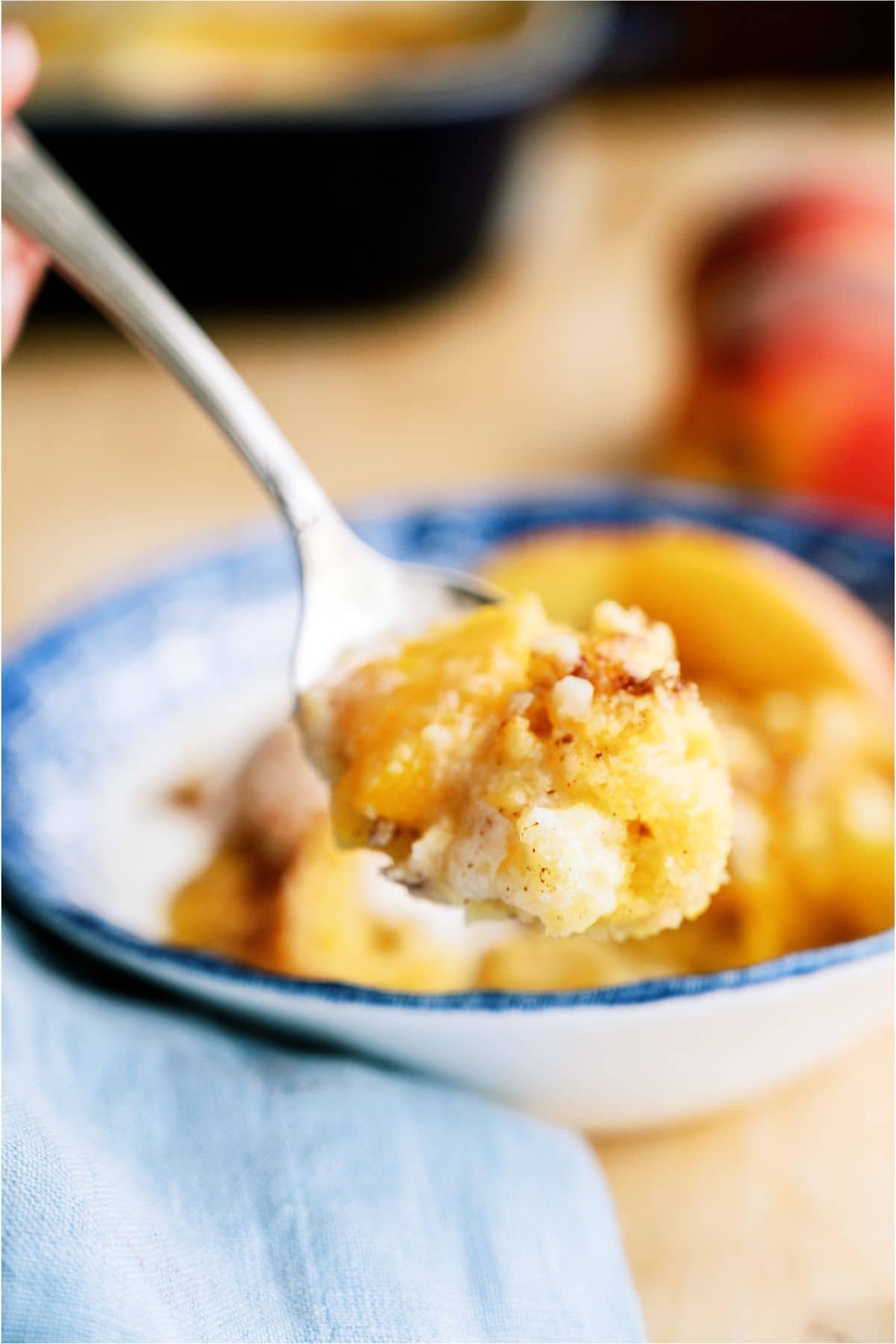 A bowl of Peach Cobbler Dump Cake (4 Ingredients) with a spoon lifting a bite out