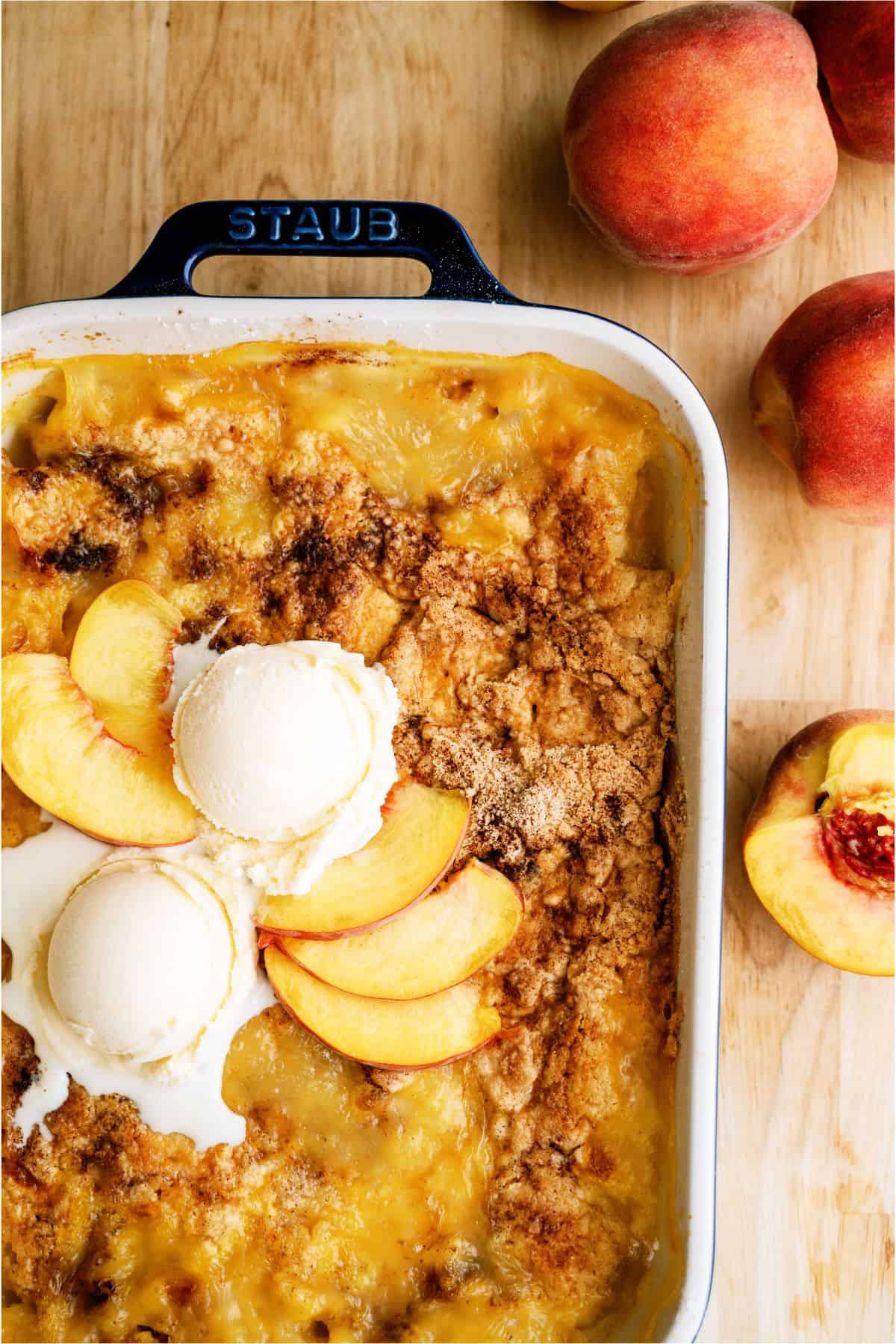 Close up of Peach Cobbler Dump Cake (4 Ingredients) in baking dish surrounded by fresh peaches