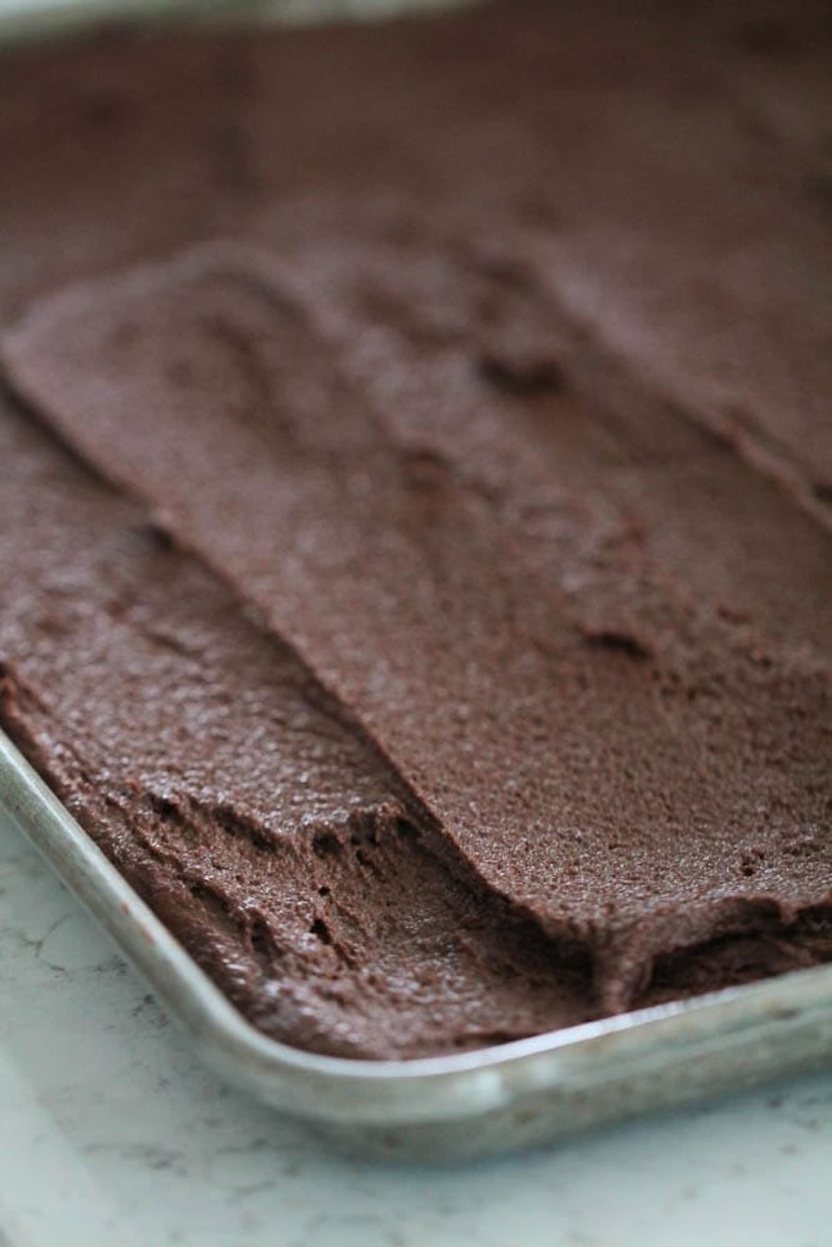 Close-up of a baking sheet covered with spread-out chocolate cake batter, ready to be baked.