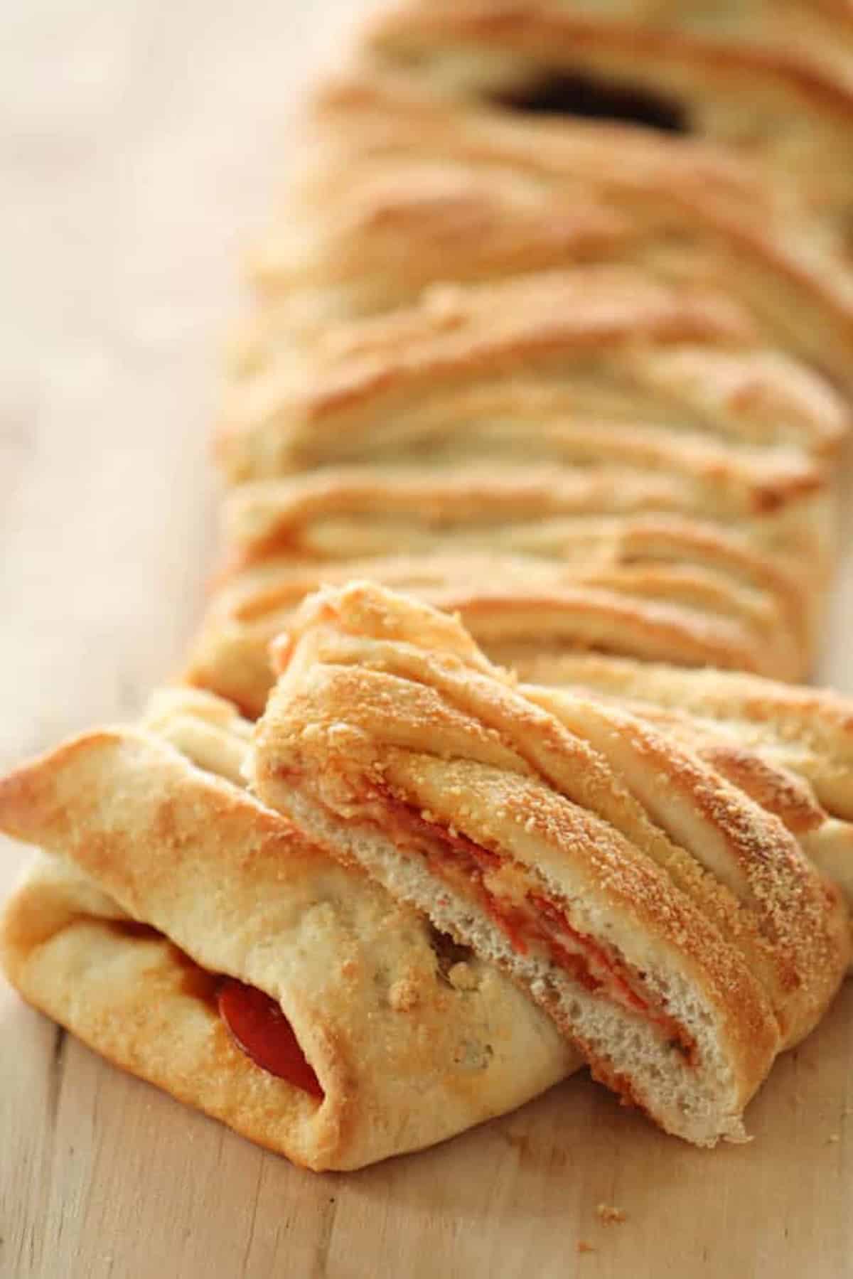 A close-up of a braided, baked bread loaf with a golden brown crust and a few visible slices showing a filling likely of cheese and tomato sauce.