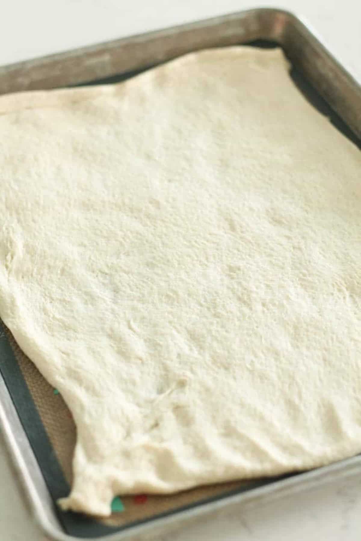 A rectangular piece of dough is spread out on a baking sheet.