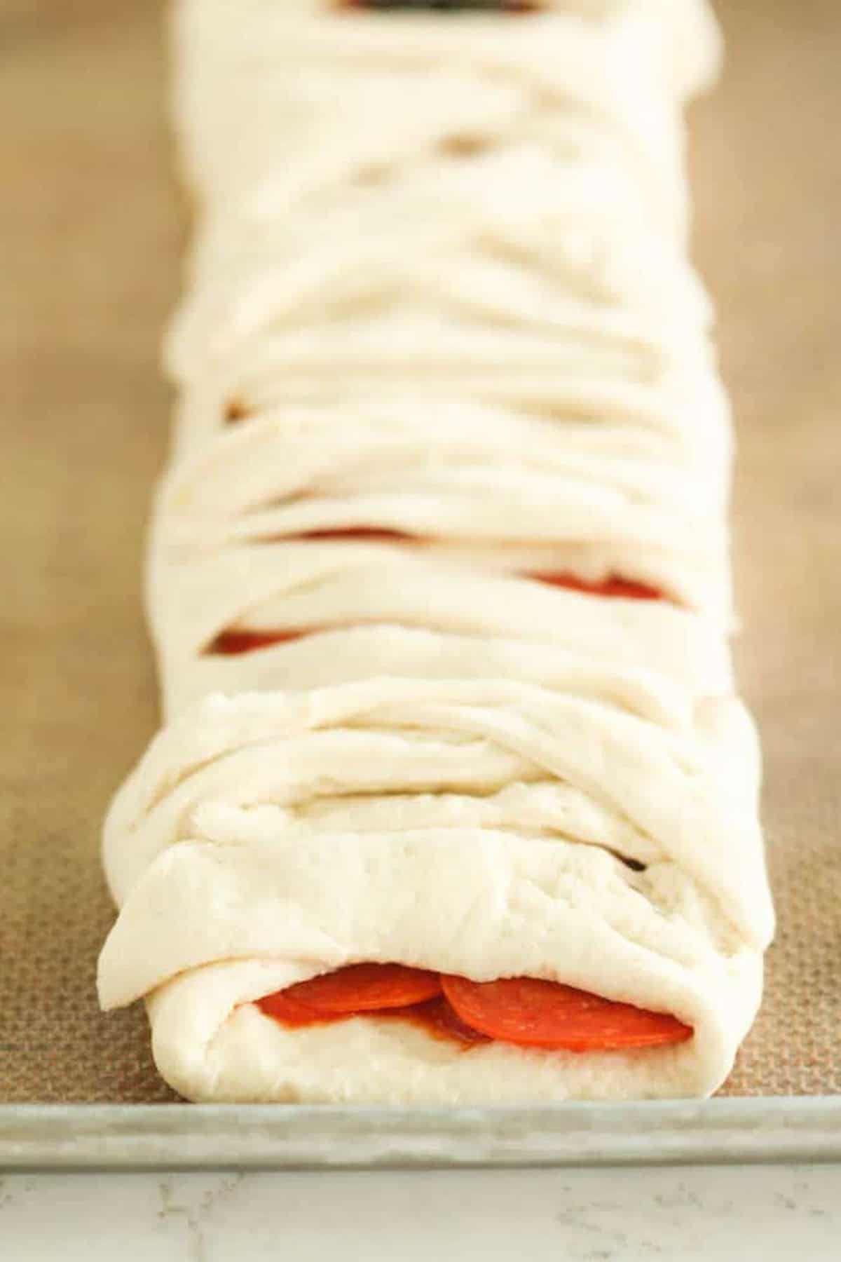 Close-up of an uncooked, braided dough with visible slices of pepperoni inside, placed on a baking sheet.