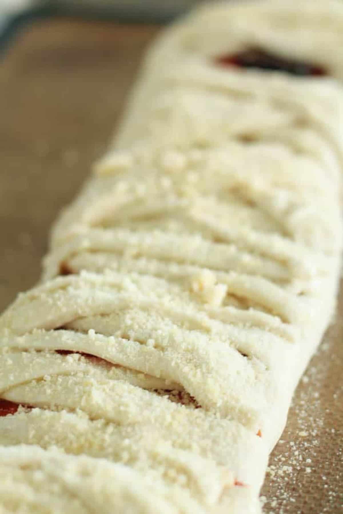 Close-up of raw, braided dough topped with grated cheese, resting on a baking tray.