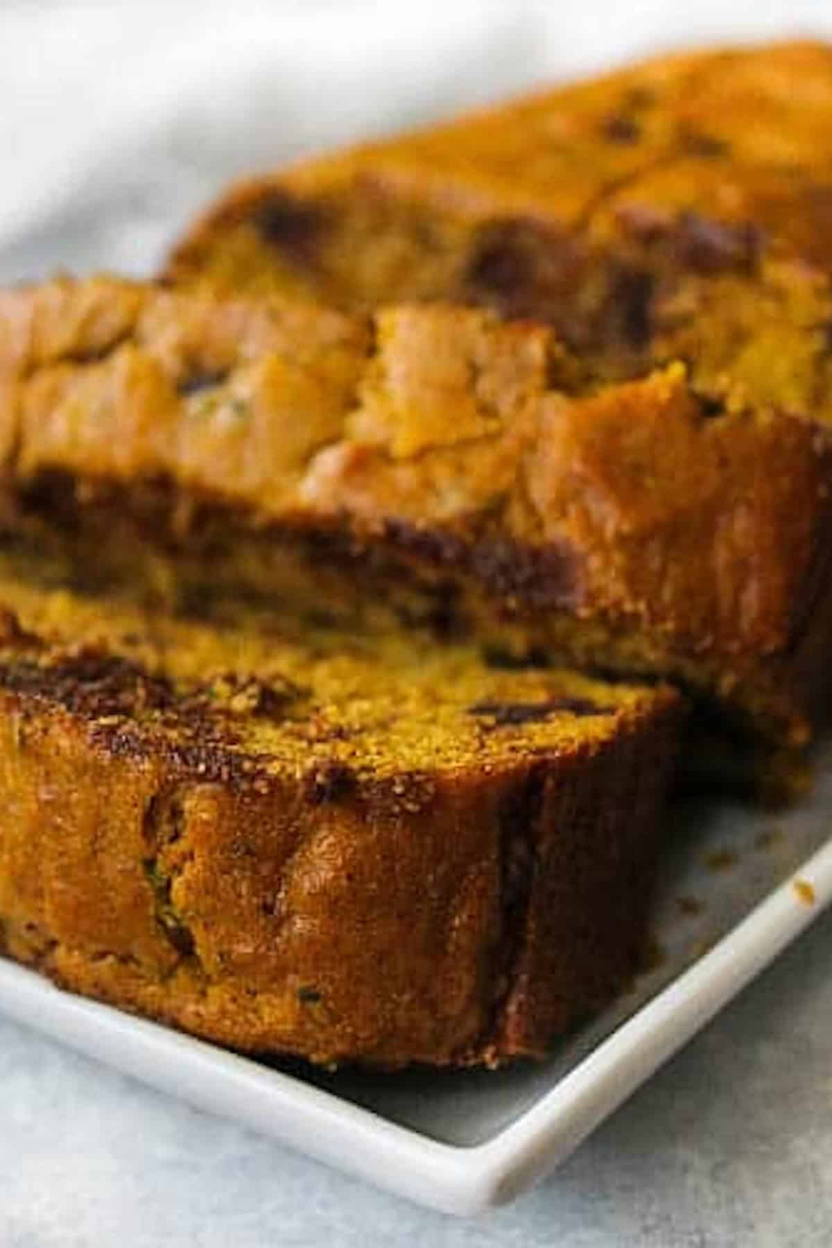 Two slices of pumpkin bread are placed on a white rectangular dish. The bread has a golden-brown crust and a moist interior.