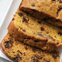 Slices of a chocolate chip pumpkin bread loaf on a white rectangular plate.