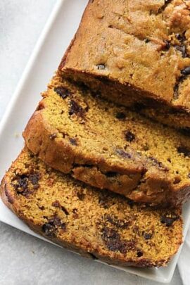 Slices of a chocolate chip pumpkin bread loaf on a white rectangular plate.