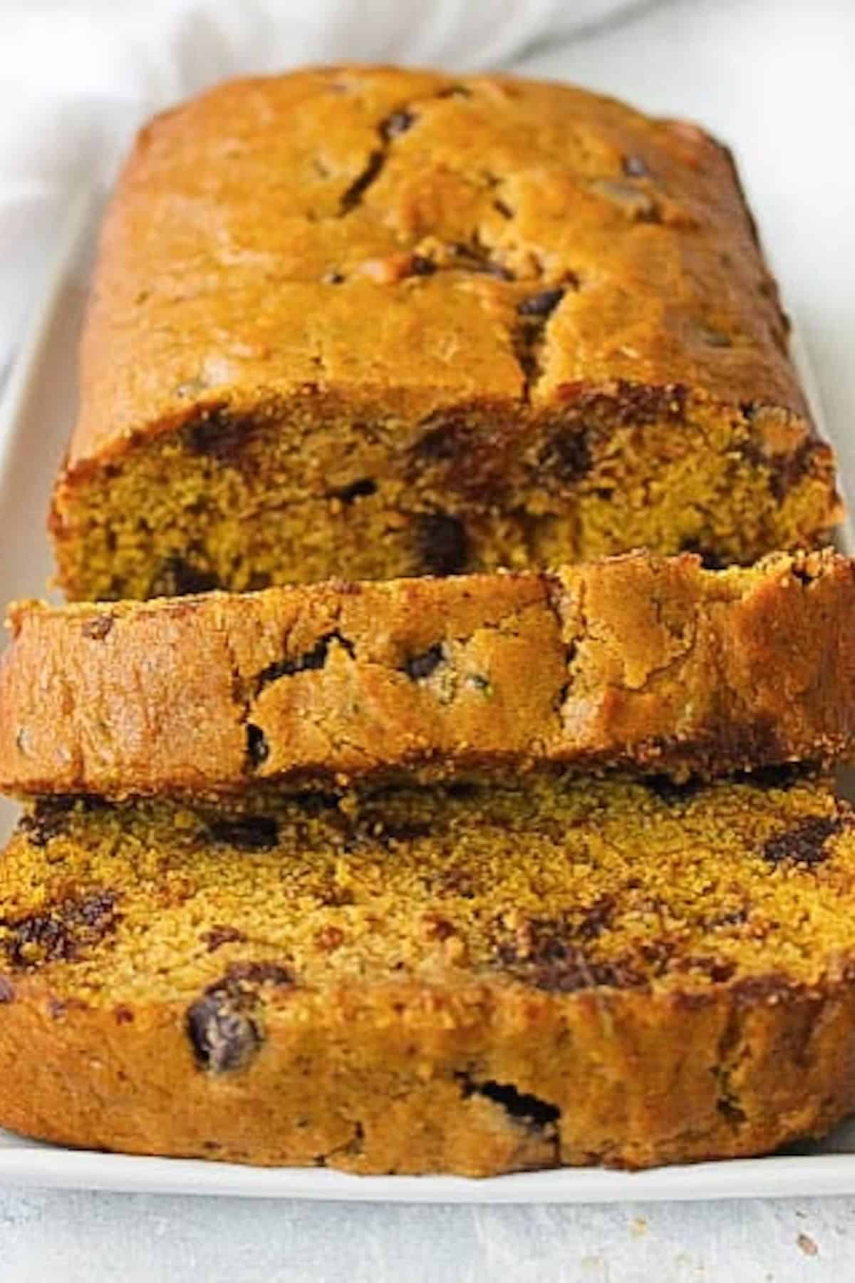 A loaf of sliced pumpkin bread with chocolate chips is displayed on a white rectangular plate.