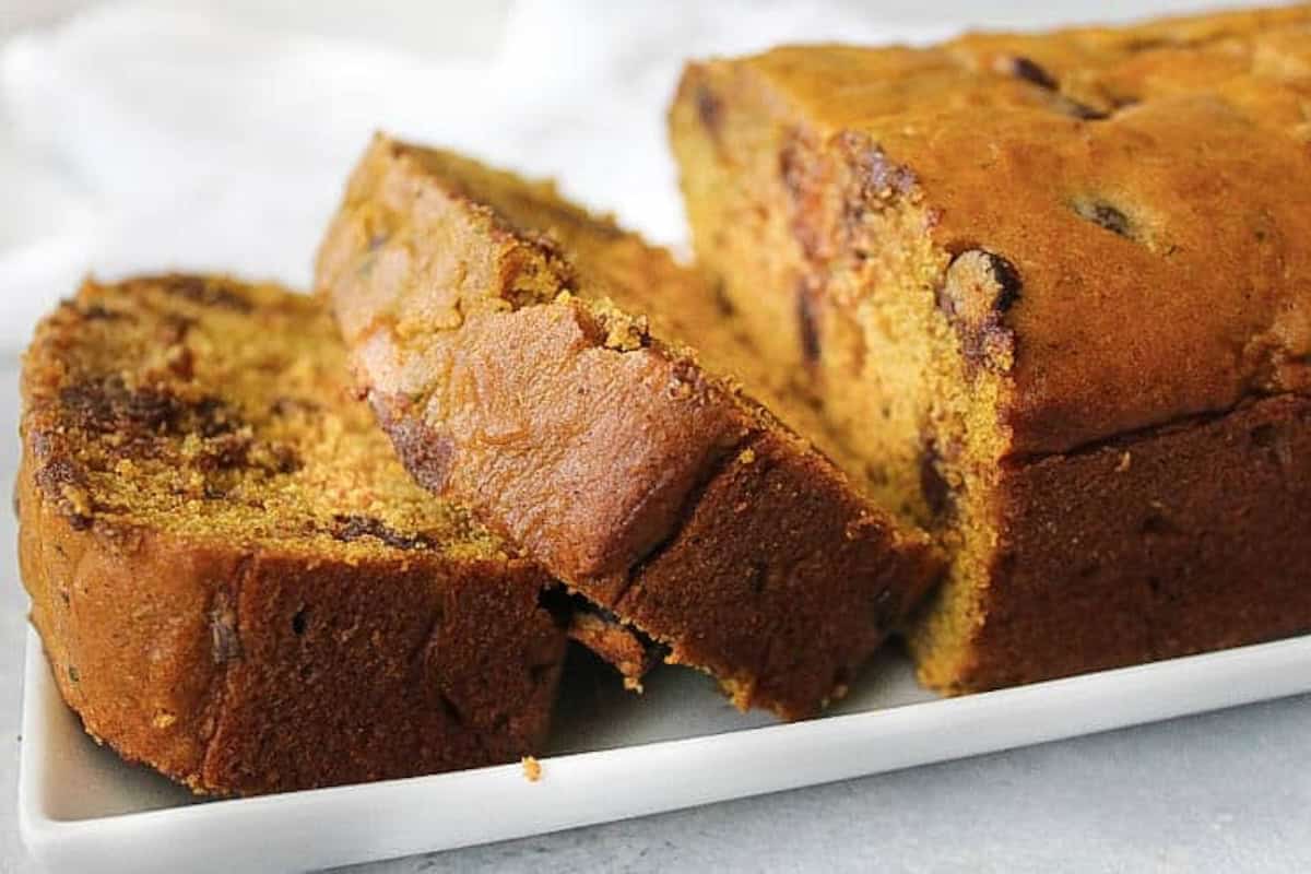 A loaf of pumpkin bread with chocolate chips is sliced and displayed on a white rectangular plate.