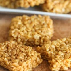 Close-up of four cereal bar squares on a wooden surface, with a few more cereal bars blurred in the background.